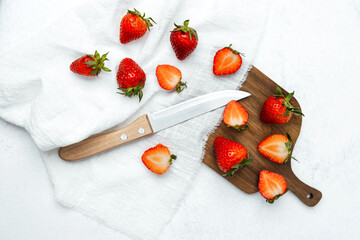 Fresh strawberries sliced on a wooden board with a knife and cloth background