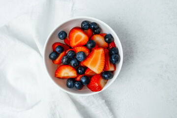 Fresh strawberries and blueberries in a bowl on a light surface