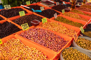Assorted olives displayed in plastic bins at Turkish outdoor market with handwritten price signs