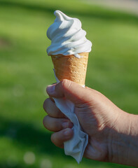 A hand holding a white ice cream cone with a napkin