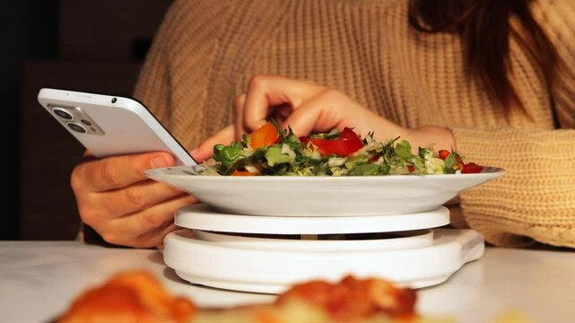 Person uses smartphone while weighing salad on a digital scale, showing technology used for healthy eating, diet, and food tracking.