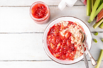 Sweet rhubarb oats in breakfast bowl Summer tasty healthy vegan food. Dietary breakfast or snack. Organic rhubarb overnight oatmeal, with rhubarb jam, yogurt, on white wooden table copy space