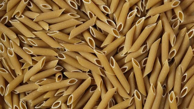 Italian spelt pasta (penne) - Penne al farro.  Uncooked Italian wholegrain Pasta. Texture, close-up. 4K Video, Rotating.