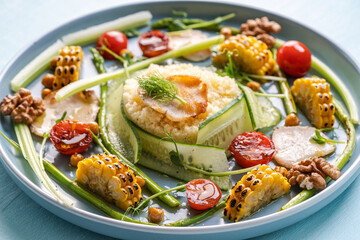 Couscous with chicken pieces, cucumbers, asparagus and corn, tomatoes and walnuts on a blue plate on a light background. Close-up.