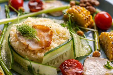 Couscous with chicken pieces, cucumbers, asparagus and corn, tomatoes and walnuts on a blue plate on a light background. Close-up.