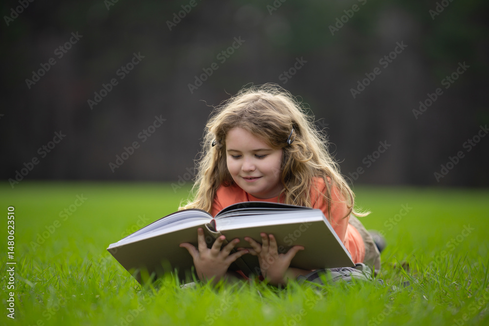 Poster child reading a book in the grass. child enjoying a book story outdoors. child studying with book in