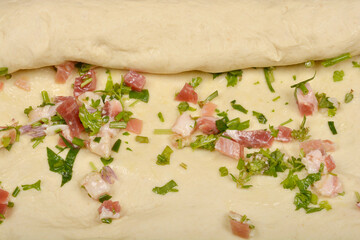 A close-up shows raw dough being rolled over a filling of diced pancetta and green herbs, preparing pancetta rolls