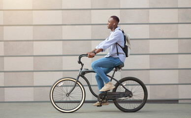 Fototapeta premium Side view of funky black guy with earphones racing on his bicycle near brick wall downtown