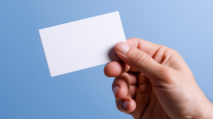 Fototapeta premium Hand holding a blank white business card against a blue background. 