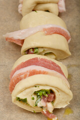 Preparation of pancetta rollsBacon-wrapped dough rolls filled with a mixture of diced pancetta and herbs are arranged on a baking sheet, ready to be baked