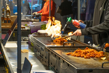 Street Food Vendor with Dynamic Energy Cooking Spicy Chicken Using Torch Flame at Night Market Stall, Seoul, South Korea, Myeongdong Market