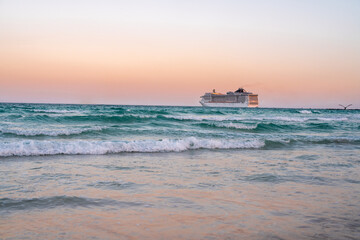 Obraz premium Cruise ship on the ocean. Luxury liner at sea. Miami Beach with cruise ship. Sea water and cruise liner. Tourist cruise ship near coast. Ocean waves and vessel boat. Summer dream vacation. Boat trip.