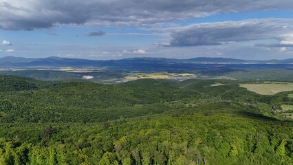 Aerial view of scenic forest-covered mountains under a sunny sky with soft clouds. Stunning natural landscape captured by drone, perfect for travel, nature, and environment themes.