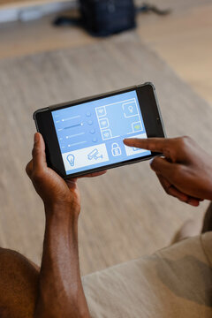 Tapping mid adult African American man using smart home interface in living room, lock icon visible