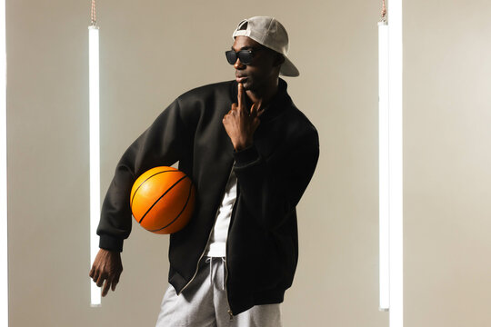 Posing African American man holding basketball in studio, with vertical light tubes