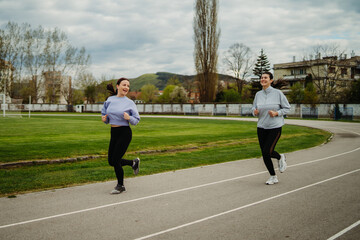 Fototapeta premium Two female friends running or jogging on stadium doing sport activities