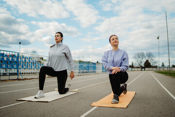Two female friends stretching on stadium doing sport activities