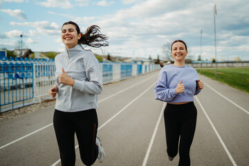 Two female friends running or jogging on stadium doing sport activities