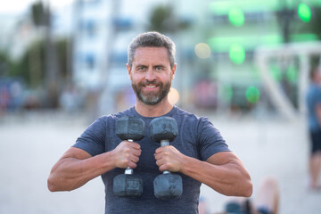 Sporty man lifting dumbbells outdoors. Fit man exercising with dumbbels in outdoor gym. Sportsman lifting dumbbells. Middle aged man training with dumbbells. Outdoor fitness training with dumbbells.