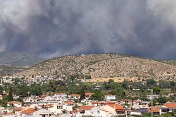 Obraz premium Heavy smoke from a large wildfire rises behind a residential town, symbolizing the environmental impact of climate change and increasing wildfire threats