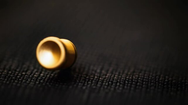 A gold metal button rests on a textured black surface in a macro shot.