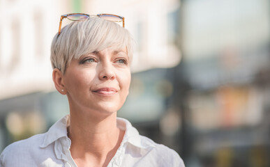 Beautiful middle aged woman with blond short hair wearing sunglasses. Profile of female person dressed in white summer shirt. Outdoors-outside