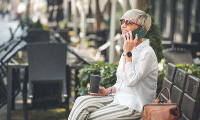 Woman on the mobile phone talking and resting on bench in the city, outdoors - outside. Profile or side view of adult female speaking on smartphone