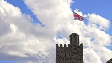 Georgian national flag waving on top of an ancient stone tower under a beautiful cloudy sky, representing Georgia's rich history and national pride