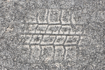 Tire track on asphalt texture. Rubber print pattern on gray concrete. Rough pavement detail. Worn out urban surface. Vehicle mark on gritty road. Grunge grained background from city street.