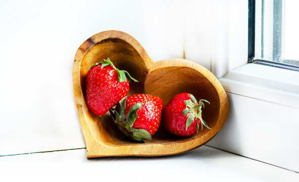 Ripe garden strawberries in a wooden heart-shaped plate on the window