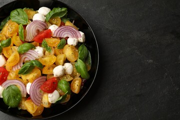 Tasty salad with yellow tomatoes, basil, onion and mozzarella cheese on black table, top view. Space for text