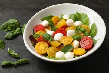 Tasty salad with yellow tomatoes, basil and mozzarella cheese on black table, closeup