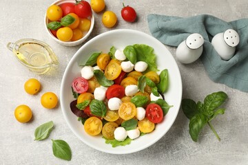 Tasty salad with yellow tomatoes, basil and mozzarella cheese on light grey table, flat lay