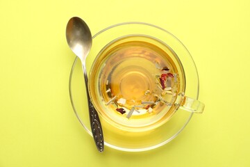 Delicious herbal tea in glass cup and spoon on green background, top view