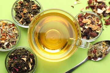 Delicious herbal tea in glass cup and dry leaves on light green background, flat lay