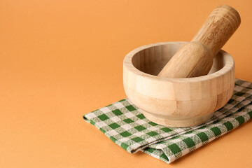 Wooden mortar, pestle and cloth on light brown background, closeup. Space for text