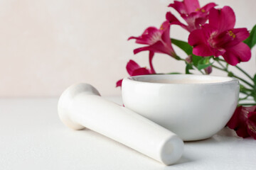 Ceramic mortar, pestle and flowers on white table, closeup