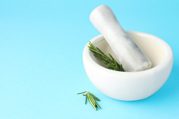 Ceramic mortar with rosemary and pestle on light blue background, closeup. Space for text