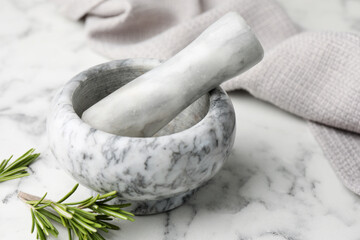 Mortar with rosemary, pestle and cloth on white marble table, closeup