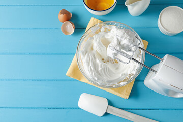 Hand mixer with whisks and whipped cream on light blue wooden table, flat lay. Space for text