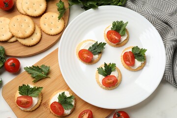 Tasty crackers with cream cheese, tomatoes and parsley on white table, flat lay