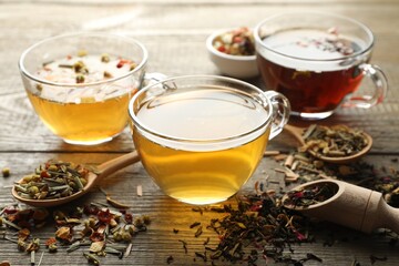 Different herbal teas and dry leaves on wooden table, closeup
