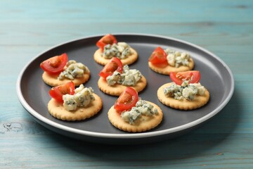 Tasty crackers with blue cheese and tomatoes on wooden table, closeup