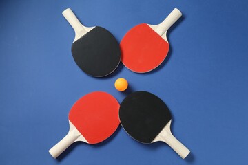 Ping pong rackets and ball on blue background, flat lay