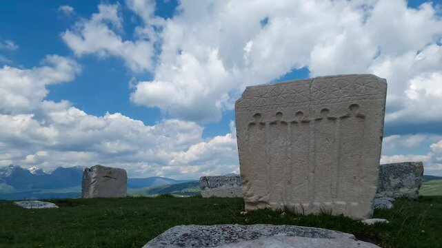 Tombstone (stećak) in ancient graveyard - stećci in medieval cemetery time lapse - historical carved stone with decoration by a grave (tomb) under dramatic sky with fast moving clouds.