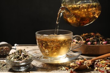 Pouring herbal tea from teapot into cup at wooden table, closeup. Space for text