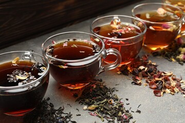 Aromatic herbal tea in glass cups and dry leaves on grey table, closeup