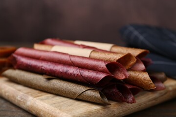 Tasty fruit leather rolls on wooden table, closeup