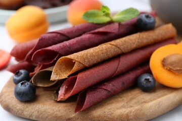Tasty candied leather rolls, fruits and berries on white table, closeup