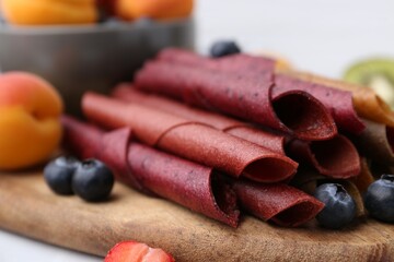 Tasty candied leather rolls, fruits and berries on white table, closeup